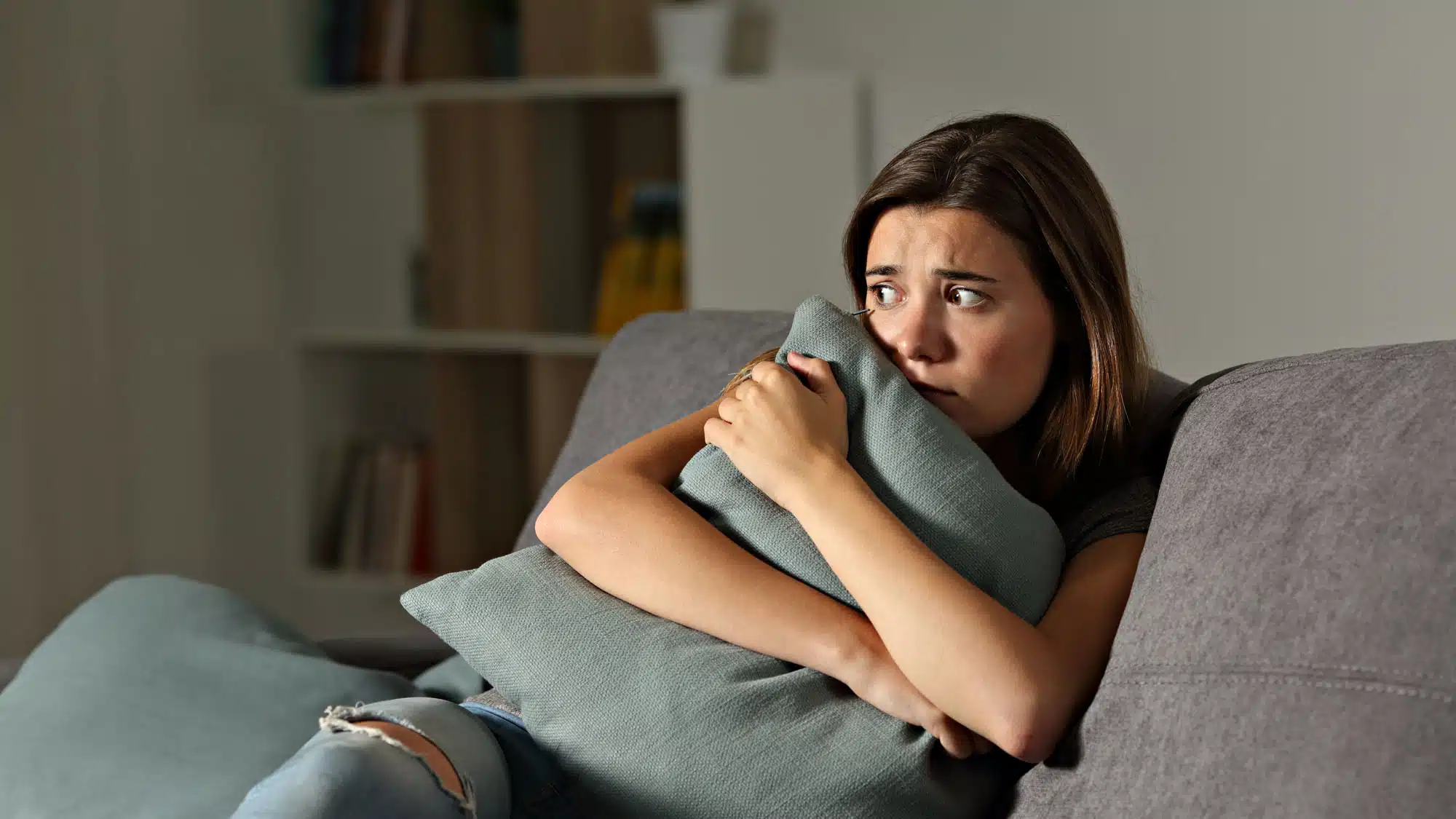 Anxious woman on couch clutching a pillow in worry