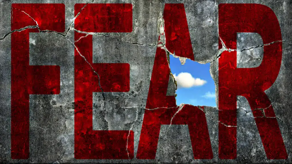 Cracked wall with red 'FEAR' revealing blue sky