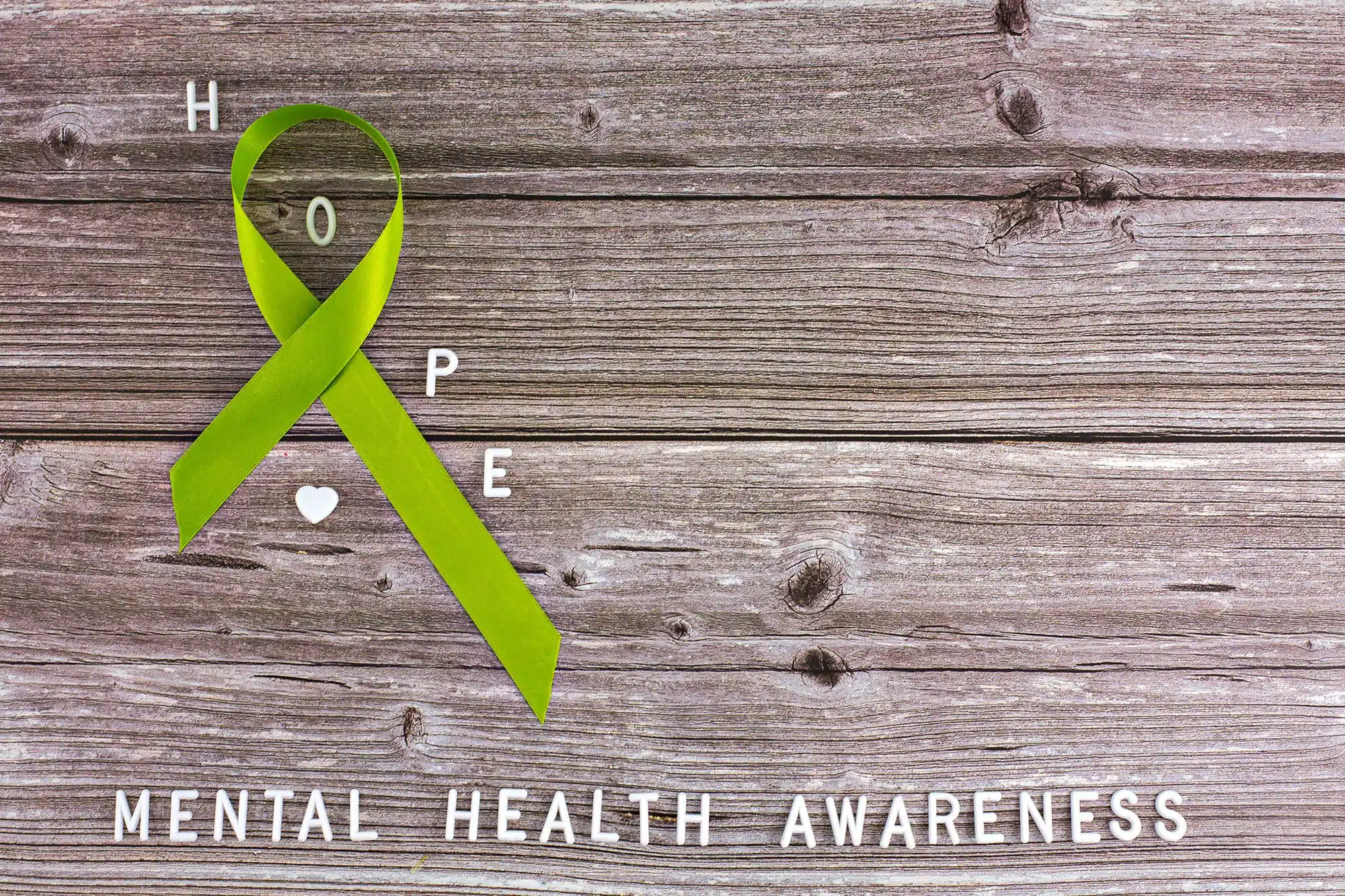 Green ribbon symbolizing mental health awareness on wooden background