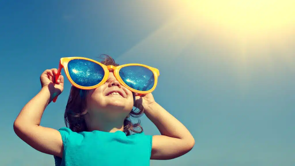 Child wearing oversized sunglasses under bright sun
