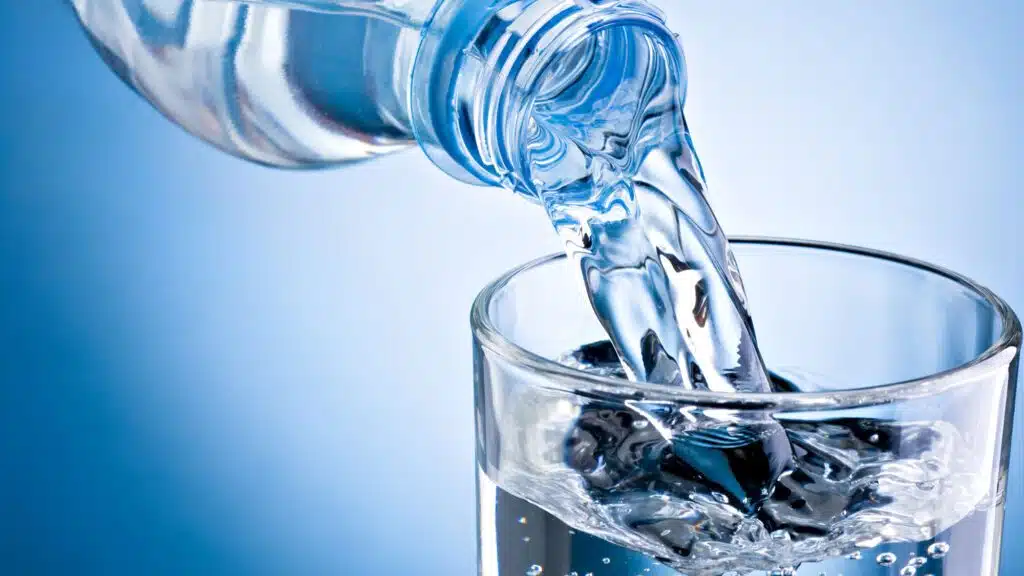 Clear bottled water pouring into glass against blue background