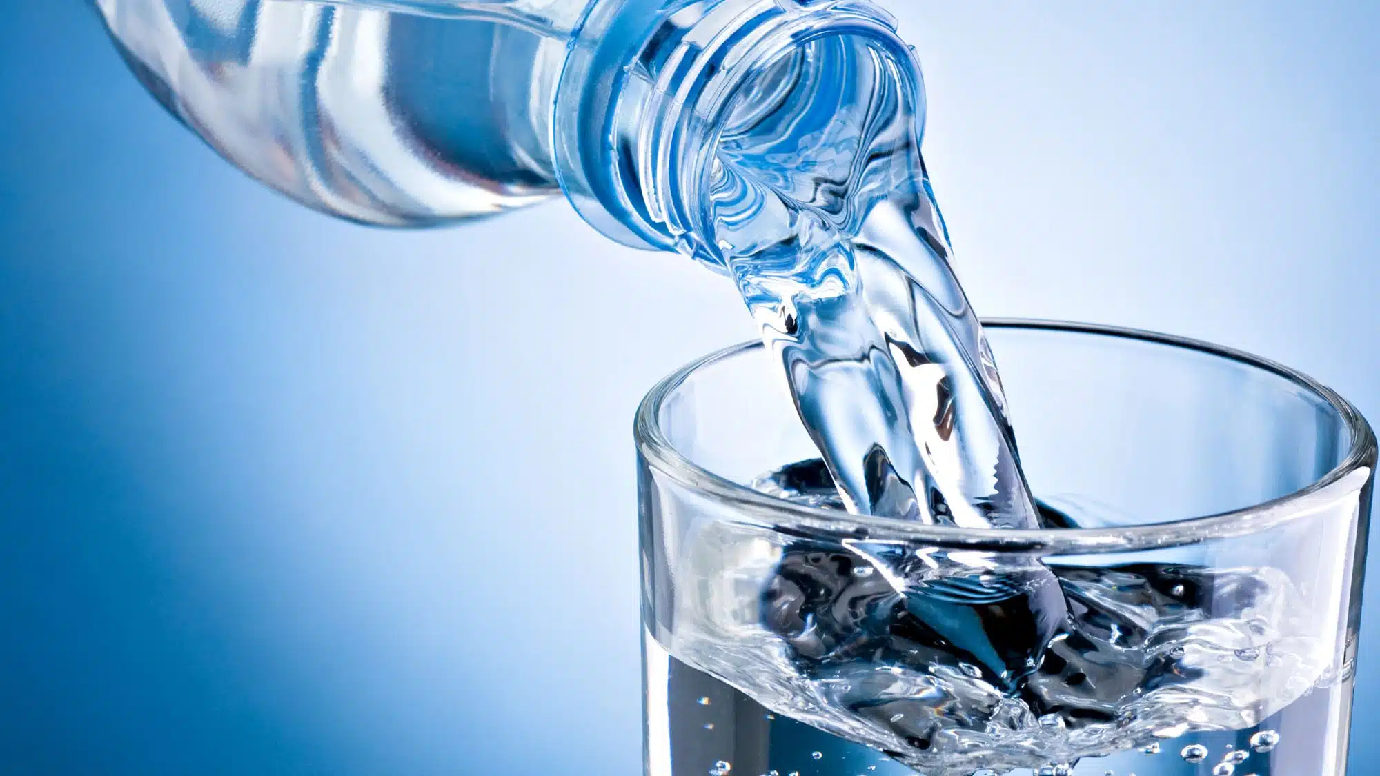 Clear bottled water pouring into glass against blue background