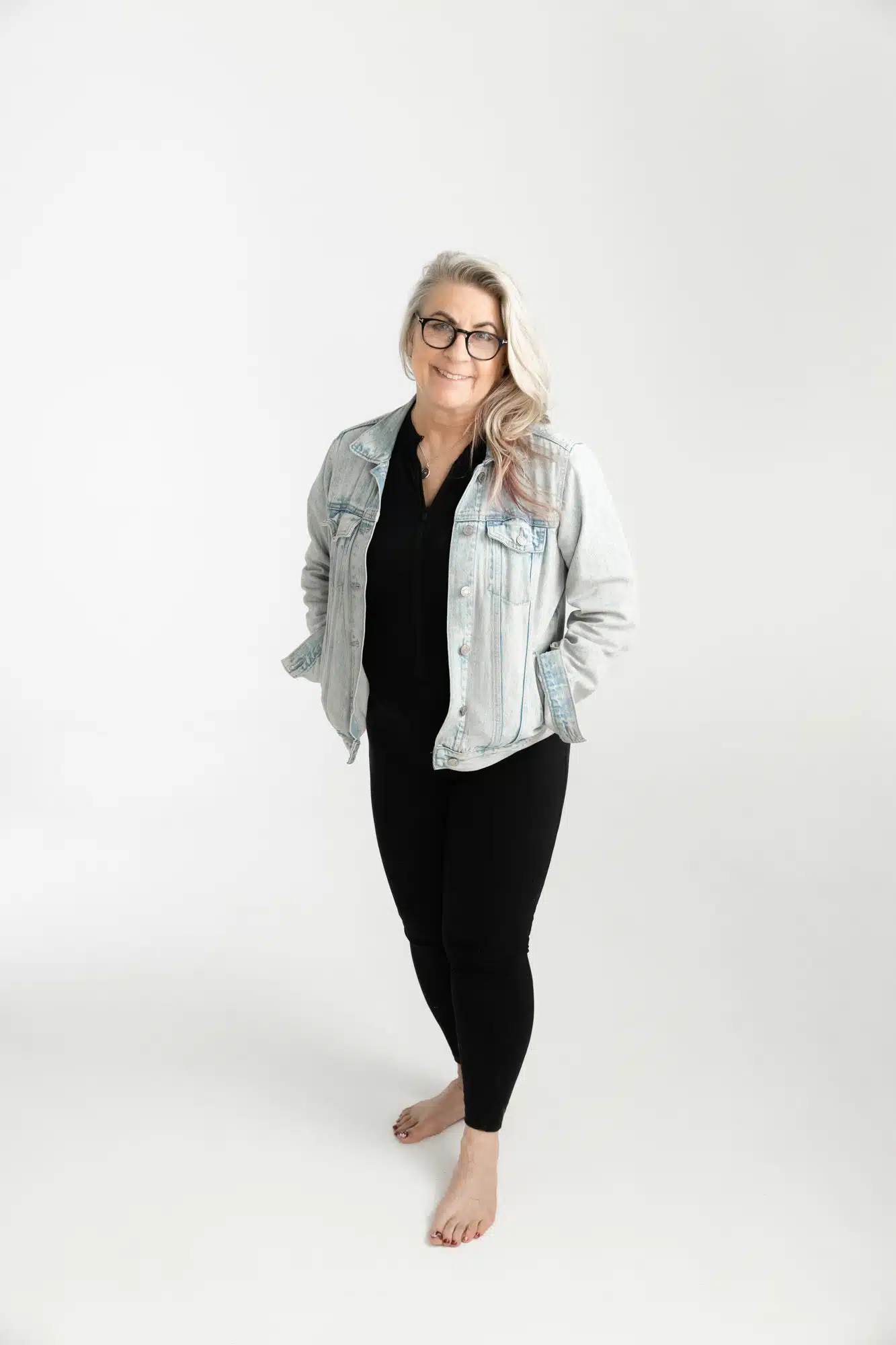 Woman in denim jacket and black outfit against white background