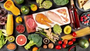 Assorted fresh food ingredients including salmon, shrimp, broccoli, and more on a dark background