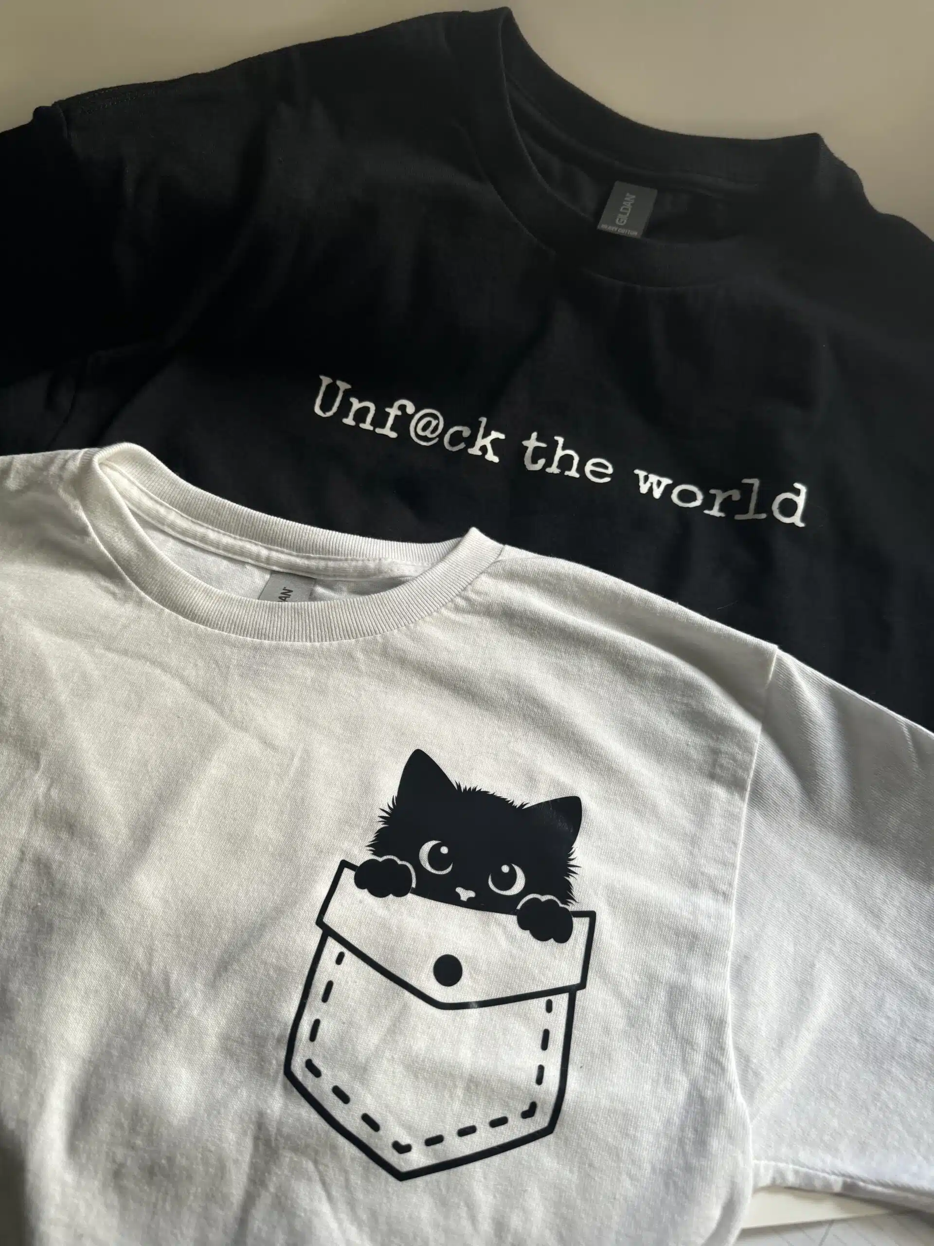 Black shirt with text and white shirt with cat in pocket design
