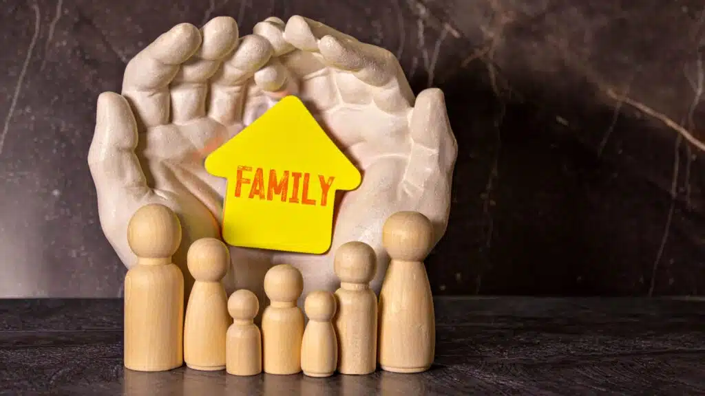 Wooden family figures with yellow house in protective hands