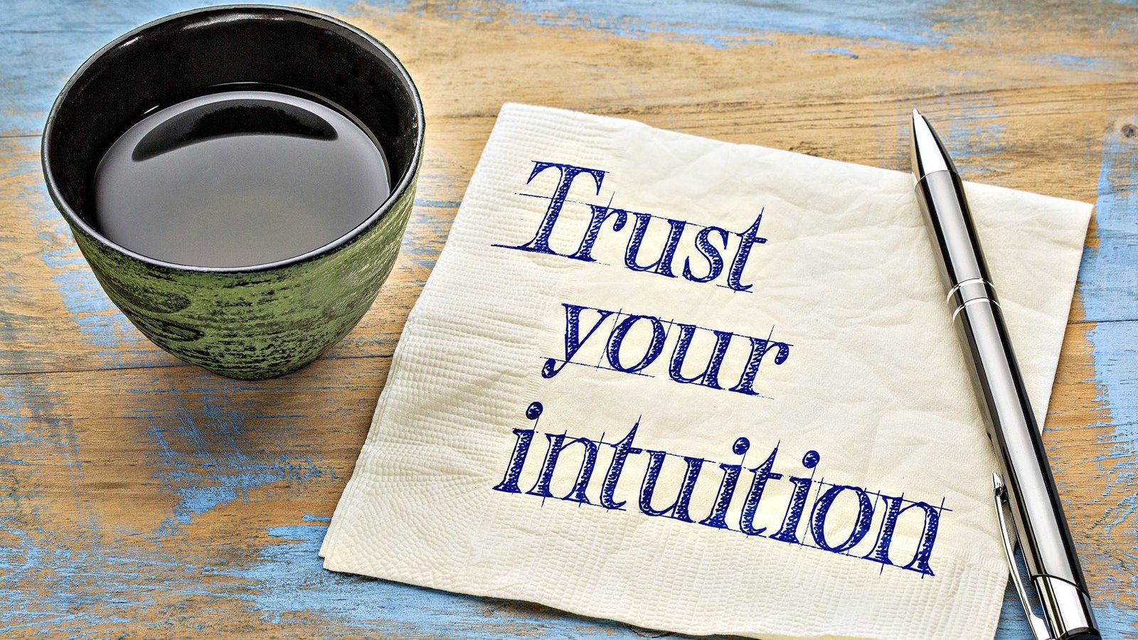 Coffee cup with pen and napkin saying Trust your intuition