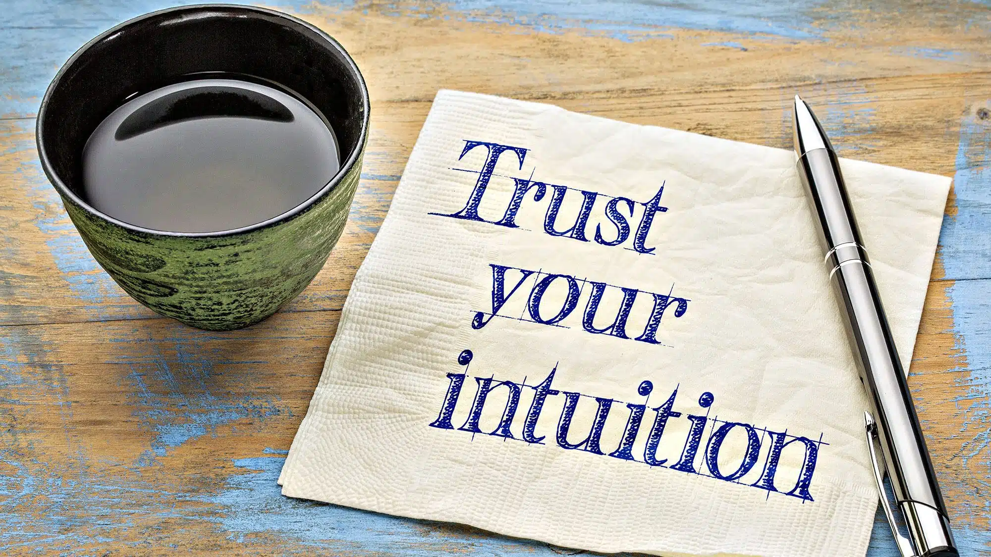 Coffee cup with pen and napkin saying Trust your intuition