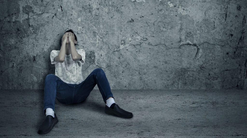 Person sitting in despair against a concrete wall