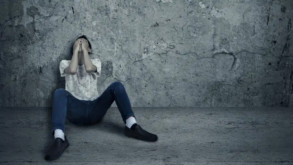 Person sitting in despair against a concrete wall