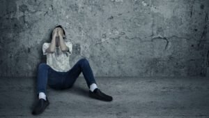 Person sitting in despair against a concrete wall