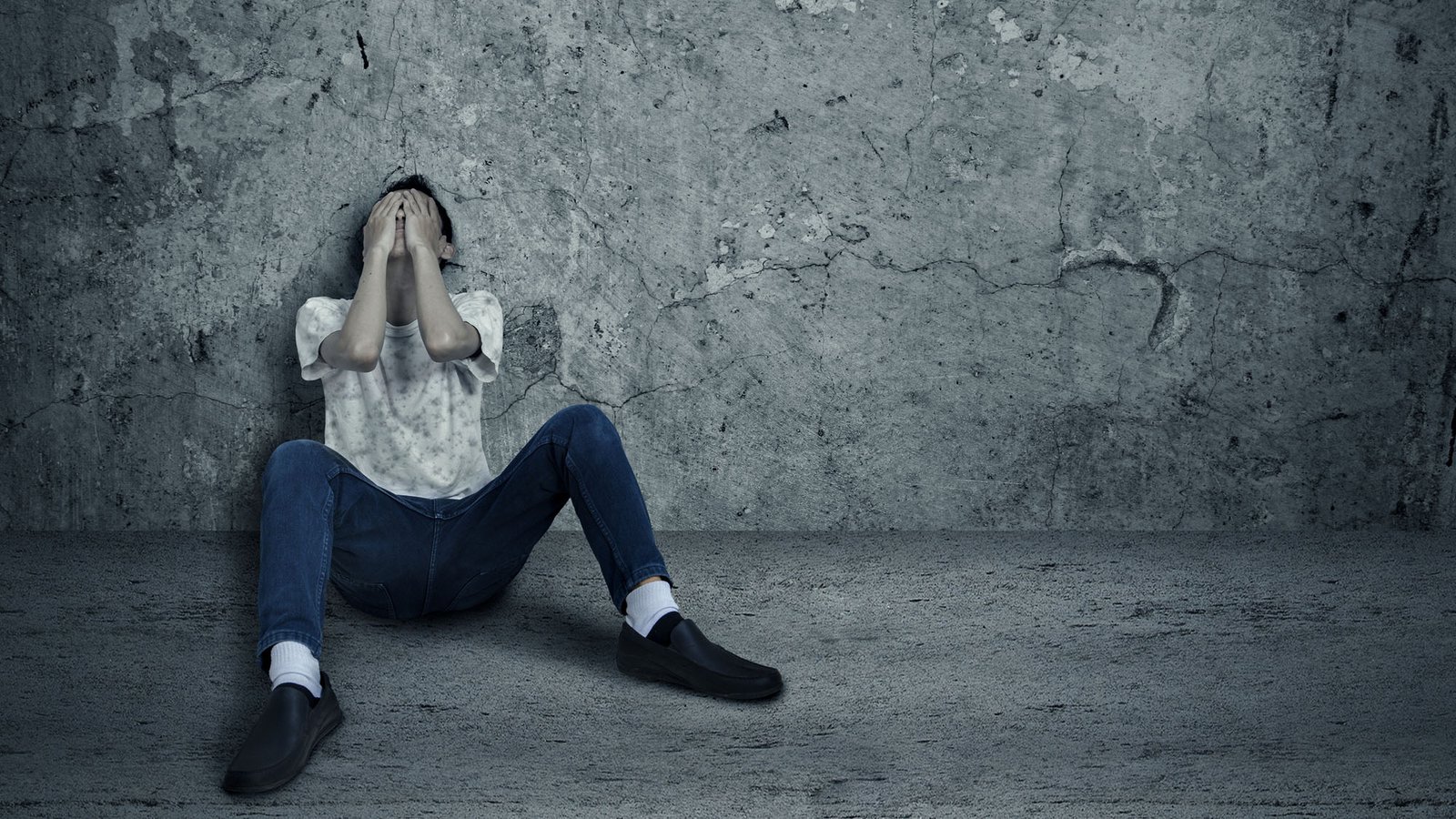 Person sitting in despair against a concrete wall