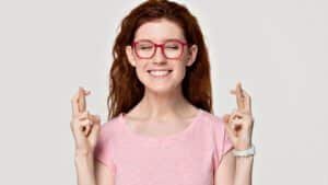 Woman with red glasses, fingers crossed, smiling