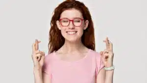 Woman with red glasses, fingers crossed, smiling