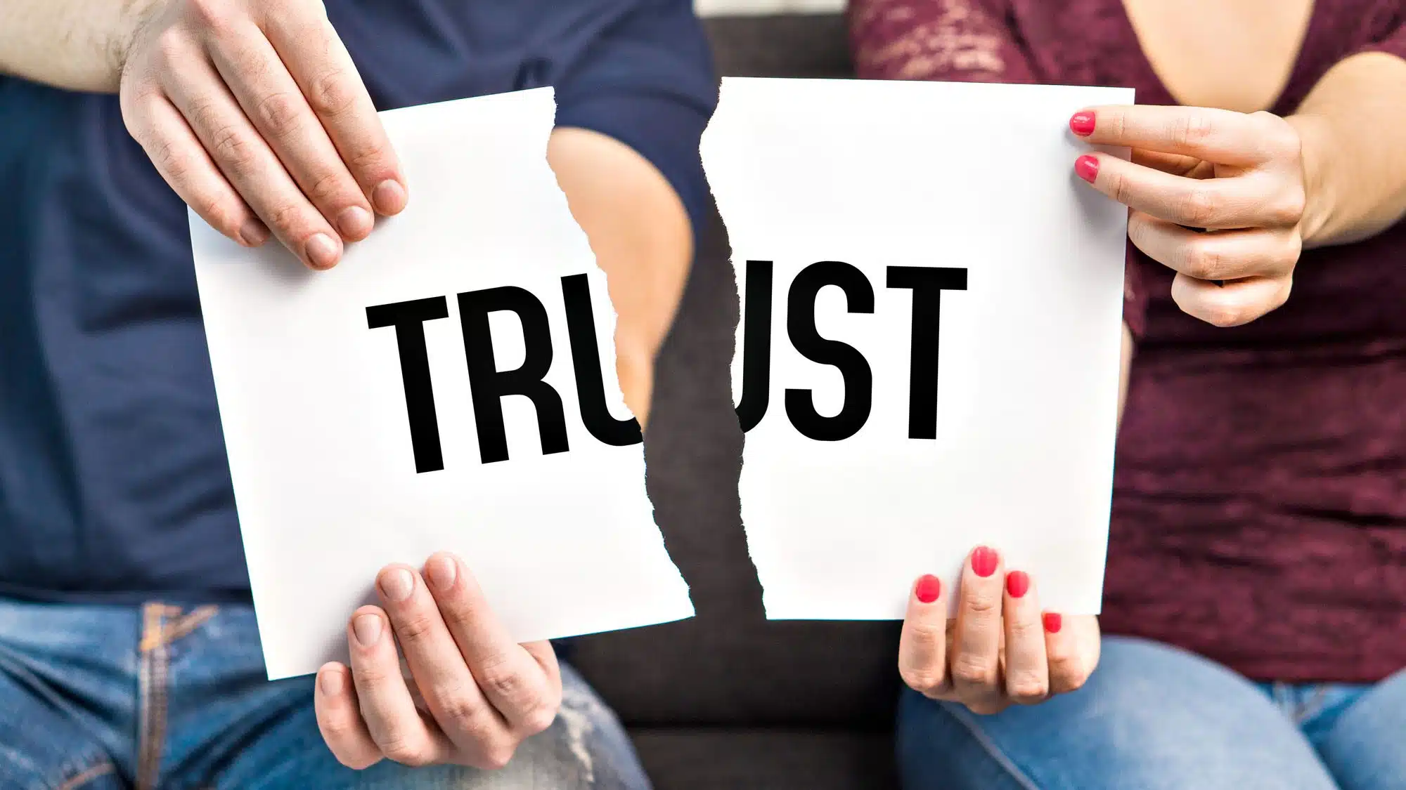 Two people tearing a paper with the word 'trust'