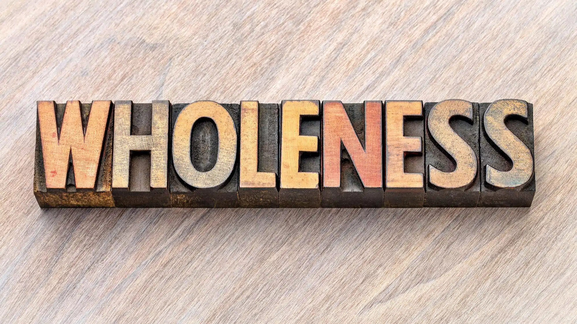 Vintage letterpress blocks spelling 'Wholeness' on wooden background