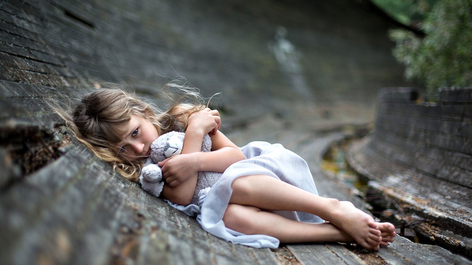 Young girl hugging a stuffed animal on a wooden pathway