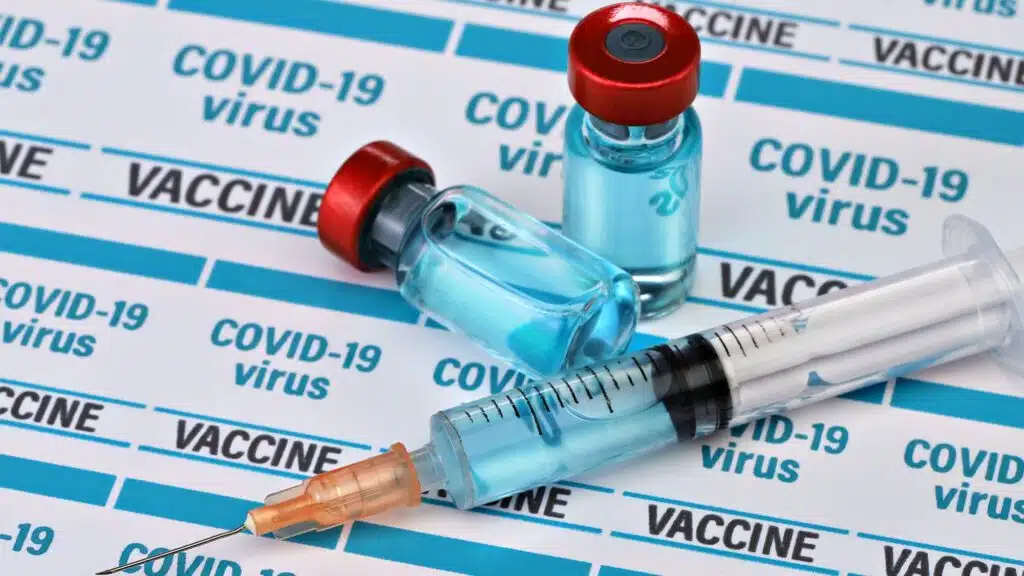COVID-19 vaccine vials and syringe on virus label background
