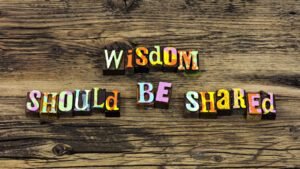 Colourful block letters spelling 'Wisdom Should Be Shared' on rustic wood
