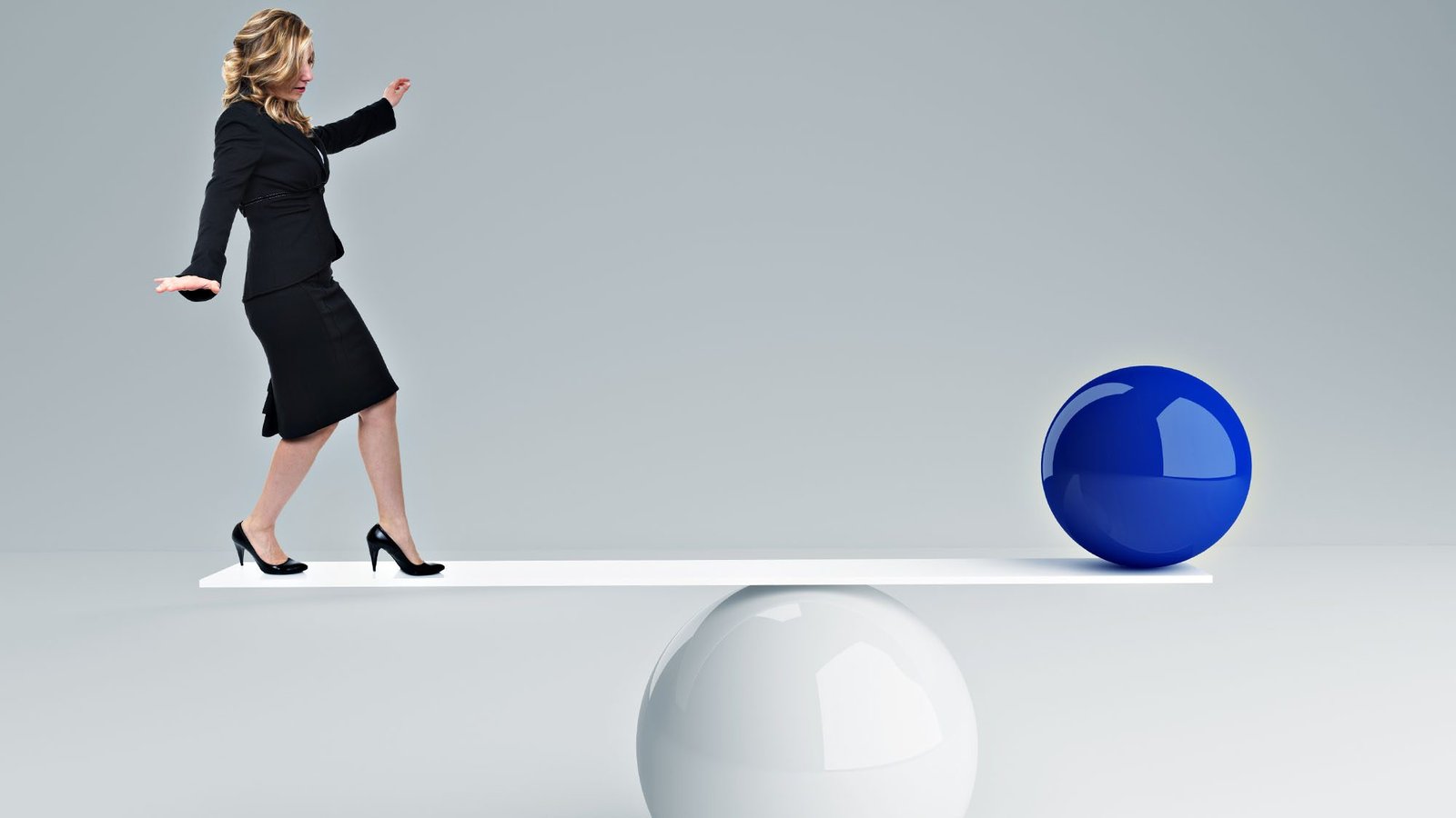 Woman in business attire balancing on plank with blue sphere