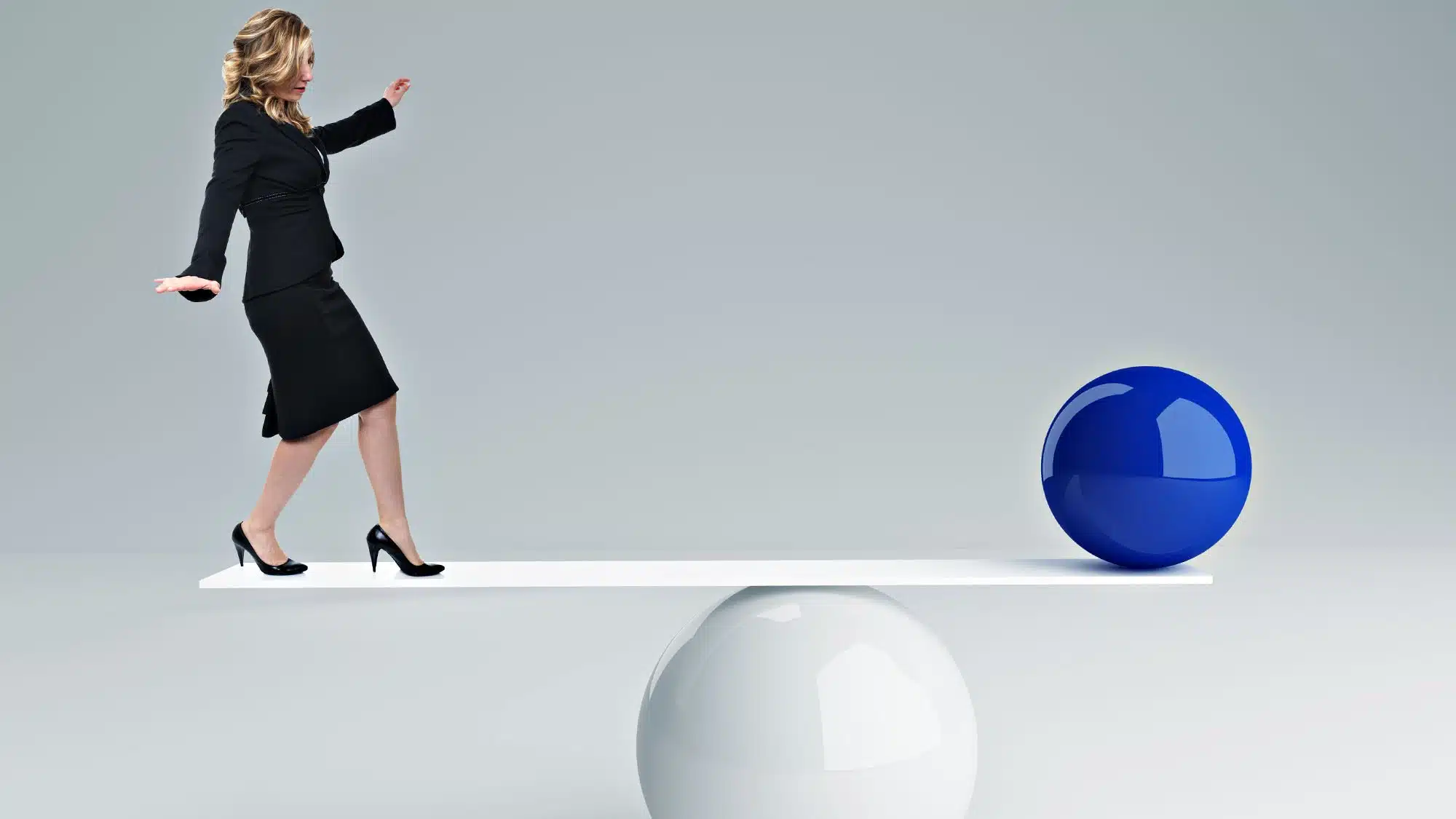 Woman in business attire balancing on plank with blue sphere