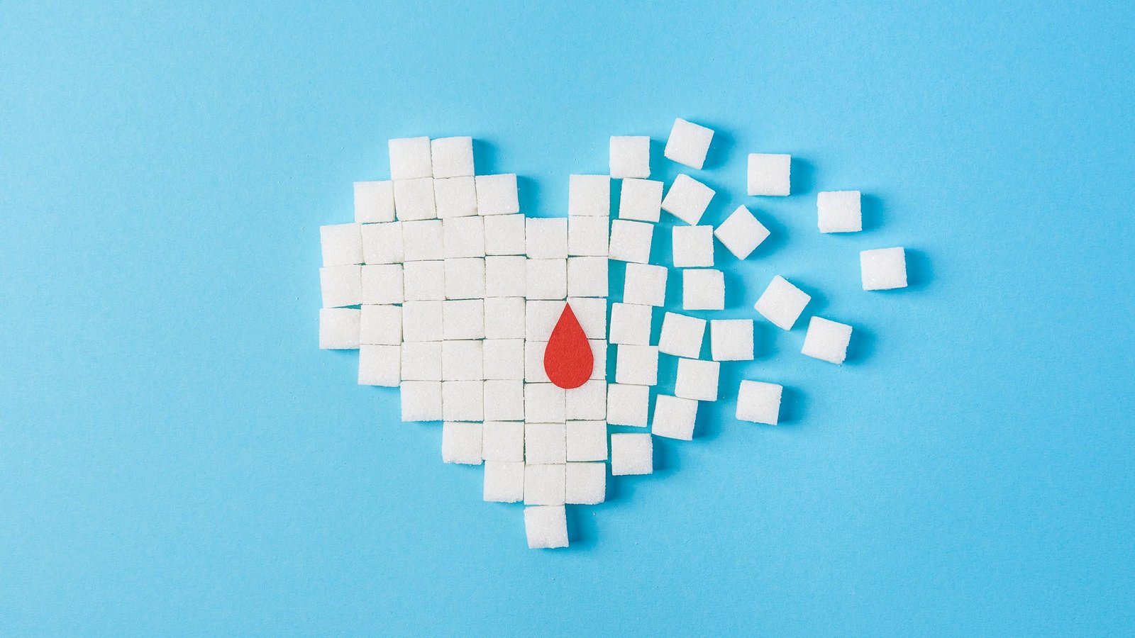 Heart made of sugar cubes dissolving with red drop on blue background