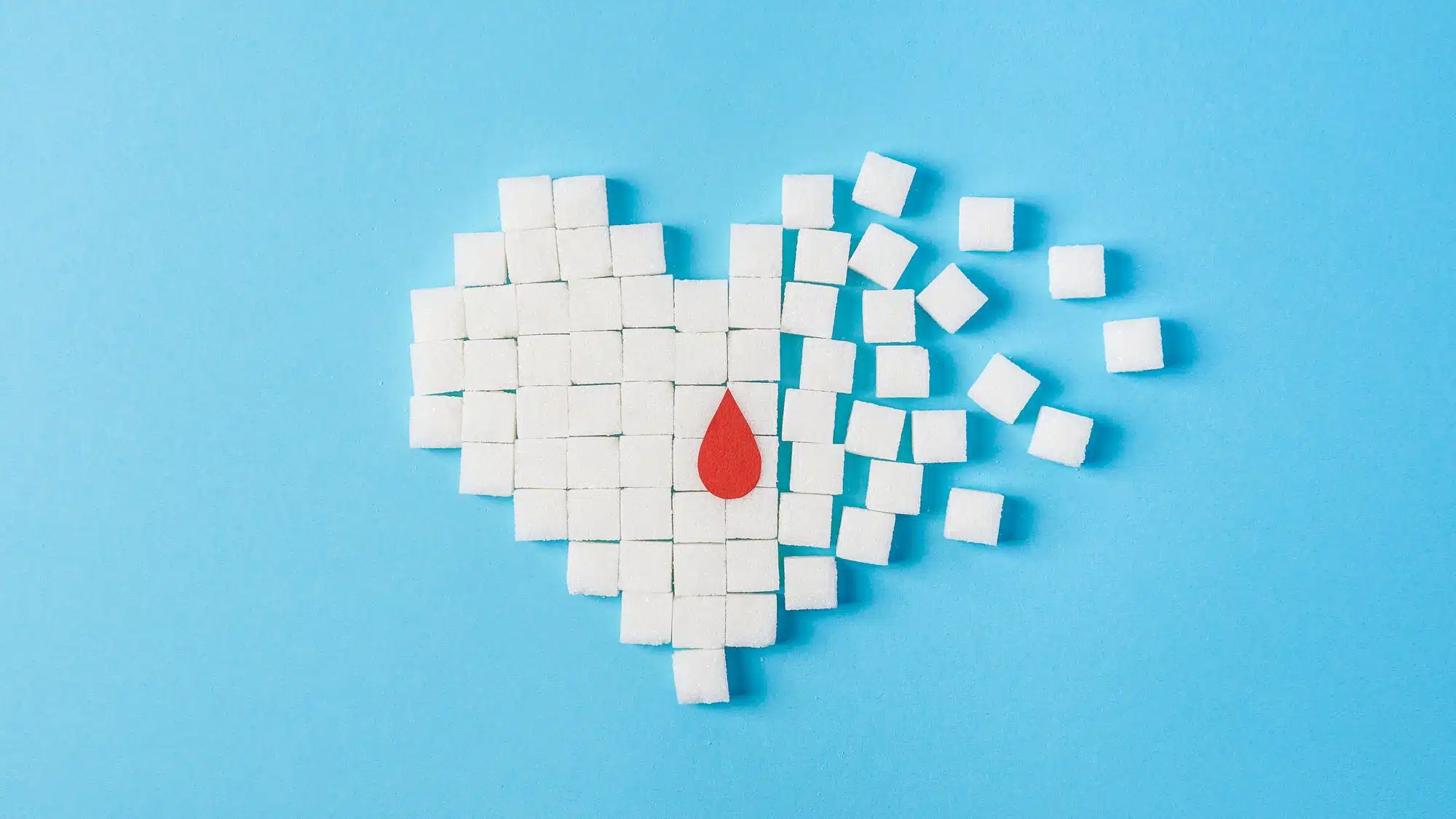 Heart made of sugar cubes dissolving with red drop on blue background