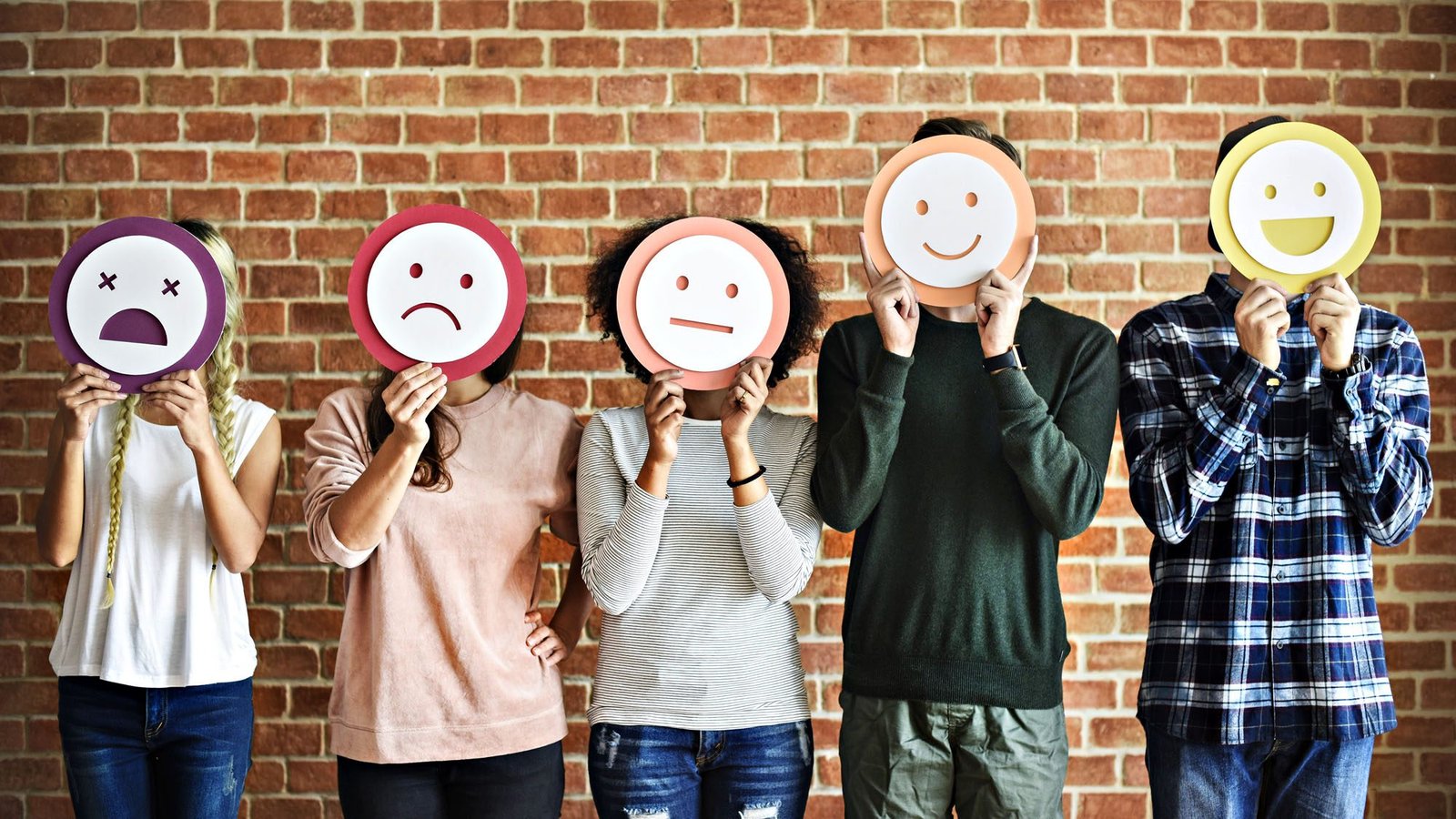 People holding emoji faces in front of brick wall background