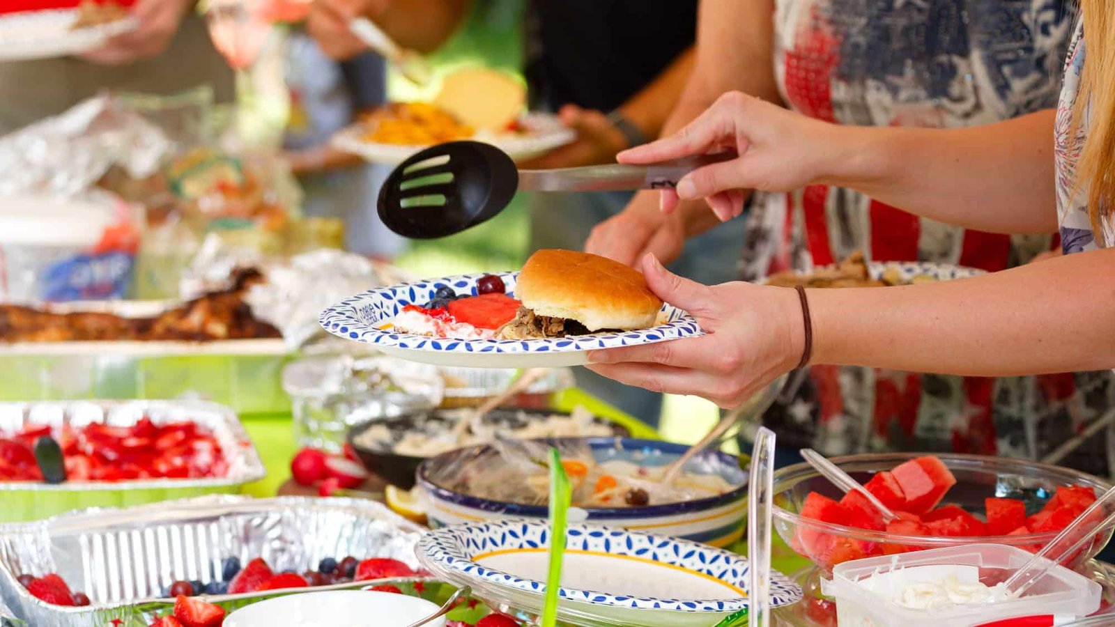 Outdoor picnic with people serving barbecue food and summer dishes