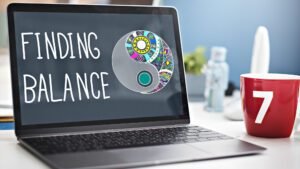Laptop displaying 'Finding Balance' with colourful yin-yang symbol and red coffee mug