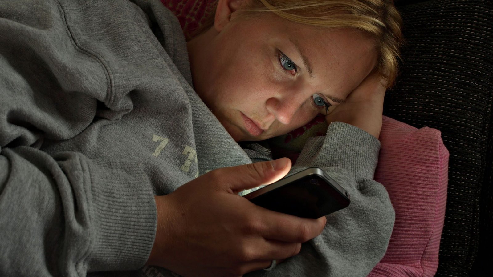Woman in hoodie using smartphone on couch, focused expression