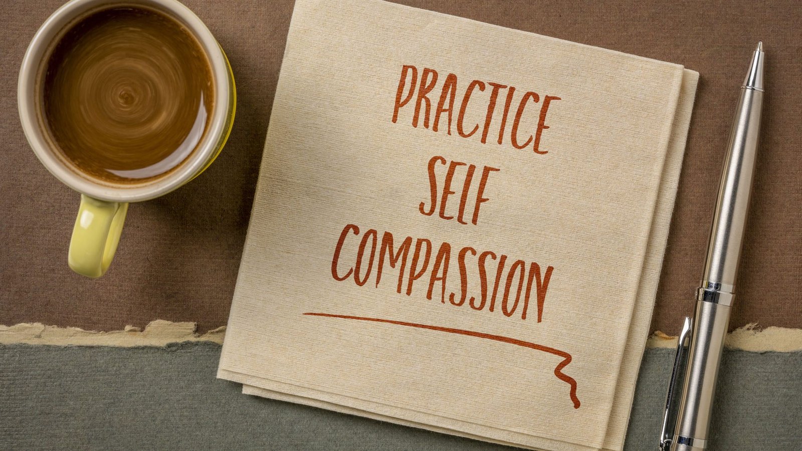 Cup of coffee, pen, and napkin with 'Practice Self-Compassion' message