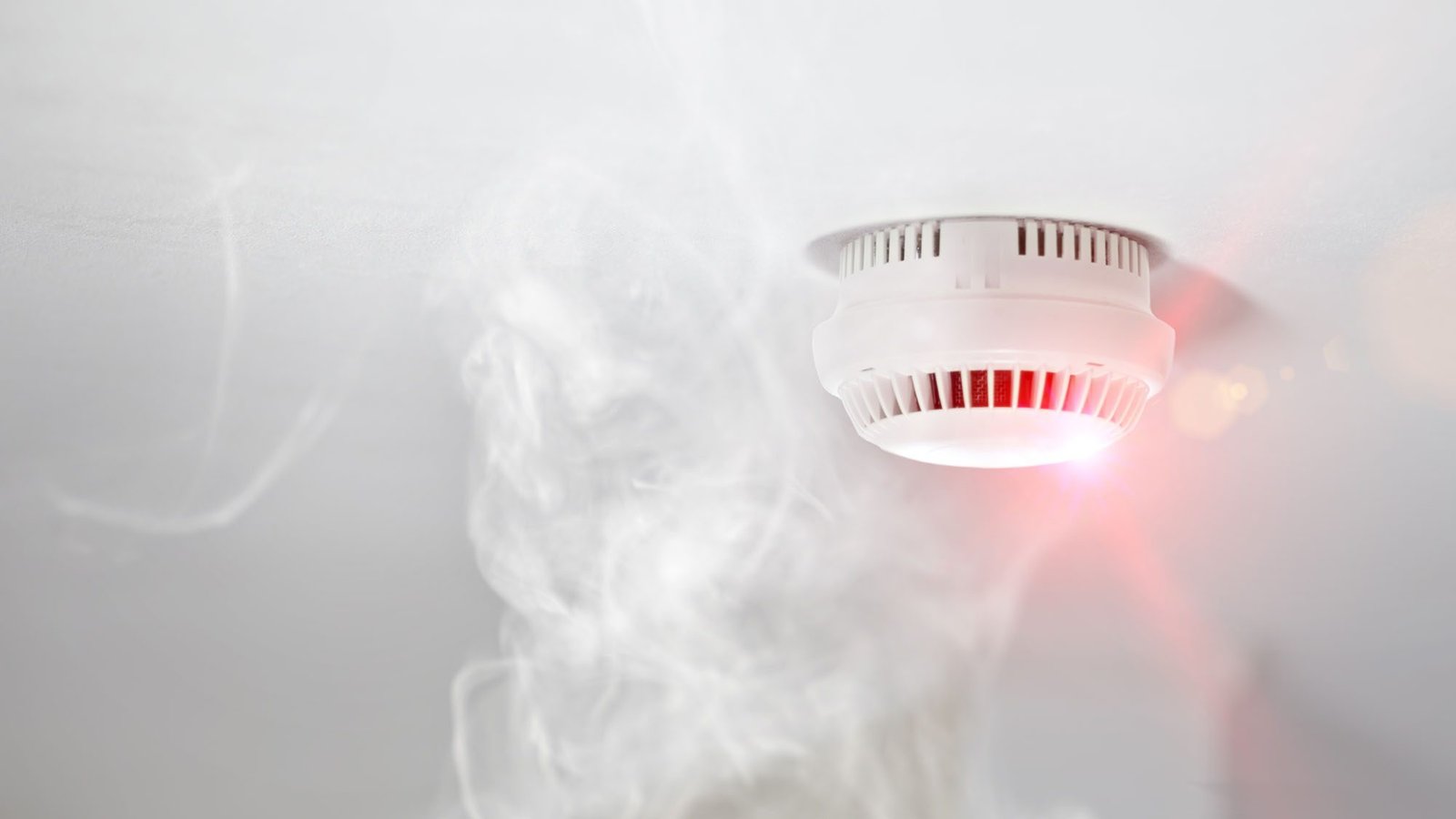 Smoke detector on ceiling with visible smoke and red light