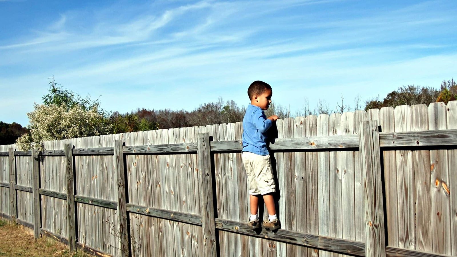 Boy climbing a wooden fence under a clear sky